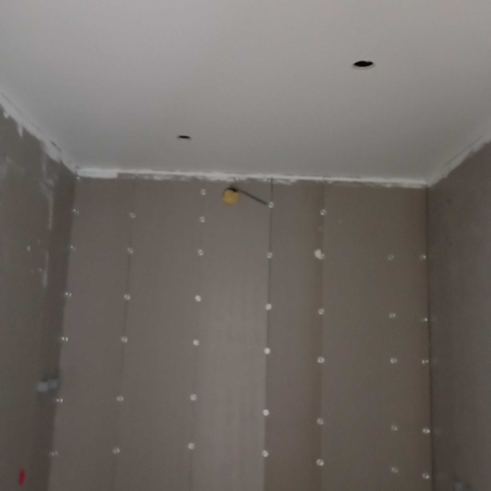 Ściany z zamontowaną płytą kartonowo-gipsową, widoczne punkty klejenia, sufit przygotowany do malowania, otwory na oświetlenie w suficie.