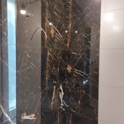 Ściana w trakcie układania płytek imitujących marmur z widocznymi kablami elektrycznymi i fragmentem białych płytek po prawej stronie.