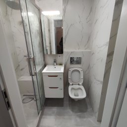 Kubatura Jakub Krzemiński - Nowoczesna łazienka z kabiną prysznicową typu walk-in, umywalką z szafką i podwieszaną toaletą, wykończona płytkami imitującymi marmur w odcieniach szarości i bieli.