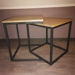 FransWeld Franciszek Nowak - Dwa stoliki kawowe z drewnianymi blatami i czarnymi metalowymi podstawami w kształcie prostopadłościanów, ustawione jeden pod drugim na drewnianej podłodze.