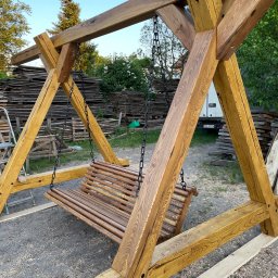 Zakład usług ogólno budowlanych Zalewski Sławomir - Drewniana huśtawka ogrodowa na łańcuchach z belek o wyraźnym usłojeniu, tło z ułożonych desek i białego busa.