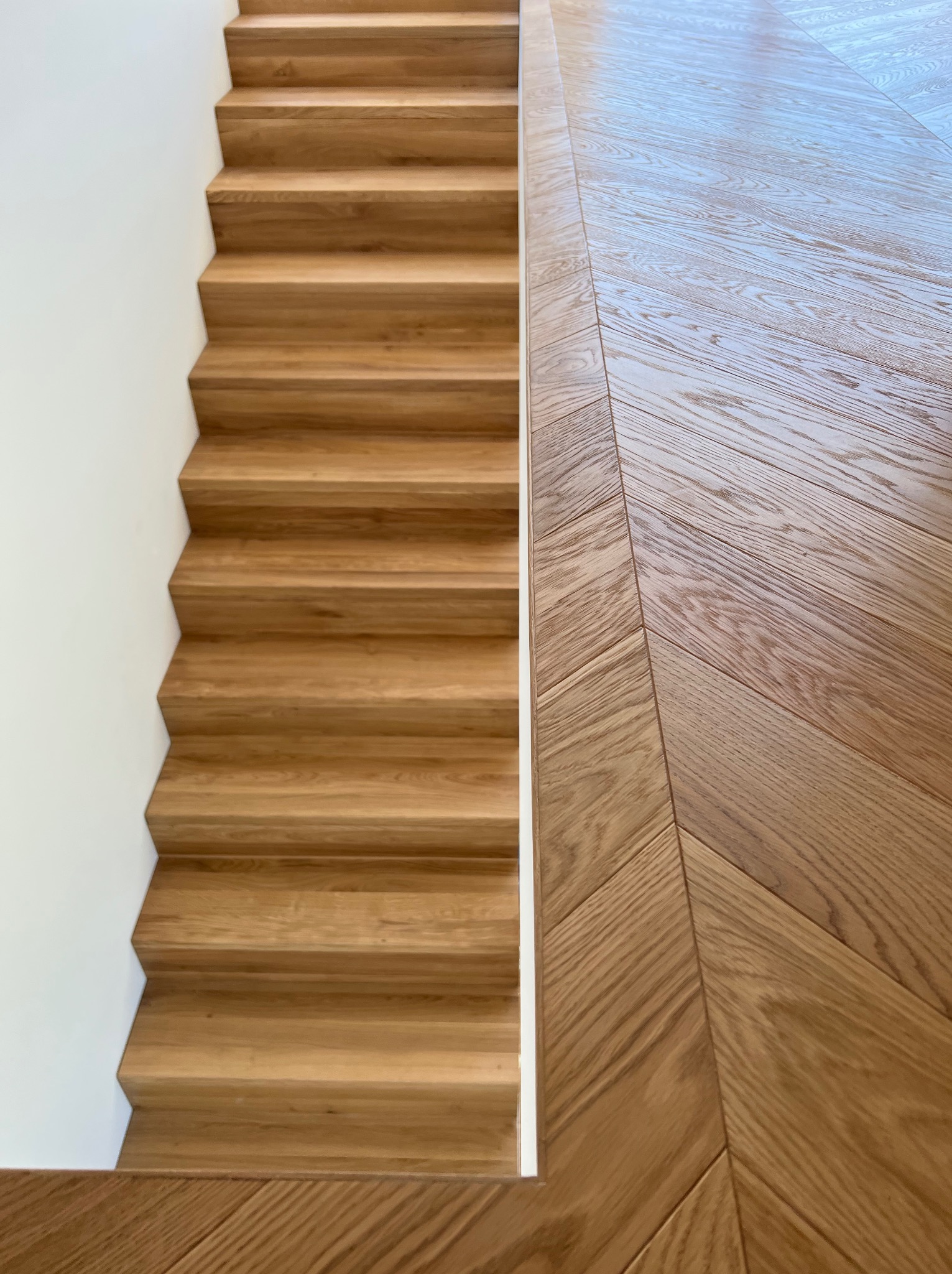 Drewniane schody z parkietem ułożonym we wzór jodełki, widok z góry, jasne oświetlenie.