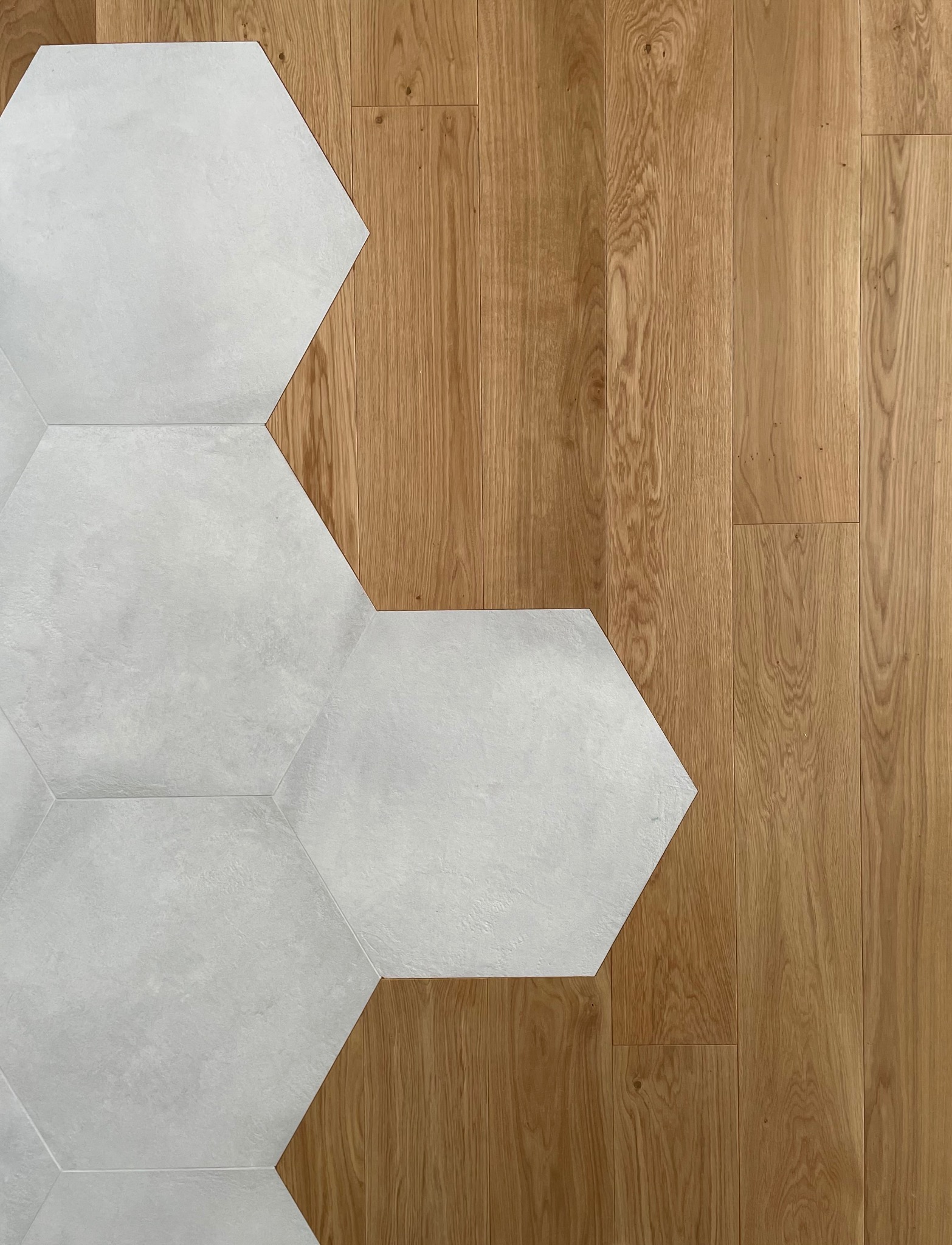 Połączenie jasnych, heksagonalnych płytek ceramicznych i podłogi z naturalnego drewna dębowego, ukazujące nowoczesny design i kontrast materiałów.
