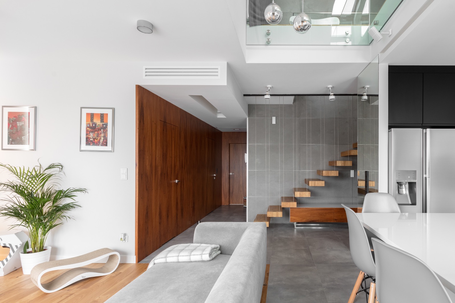 Nowoczesne wnętrze z drewnianymi schodami wiszącymi, szarą płytką ścienną, drewnianą zabudową i jasną podłogą, oświetlone kulistymi lampami.