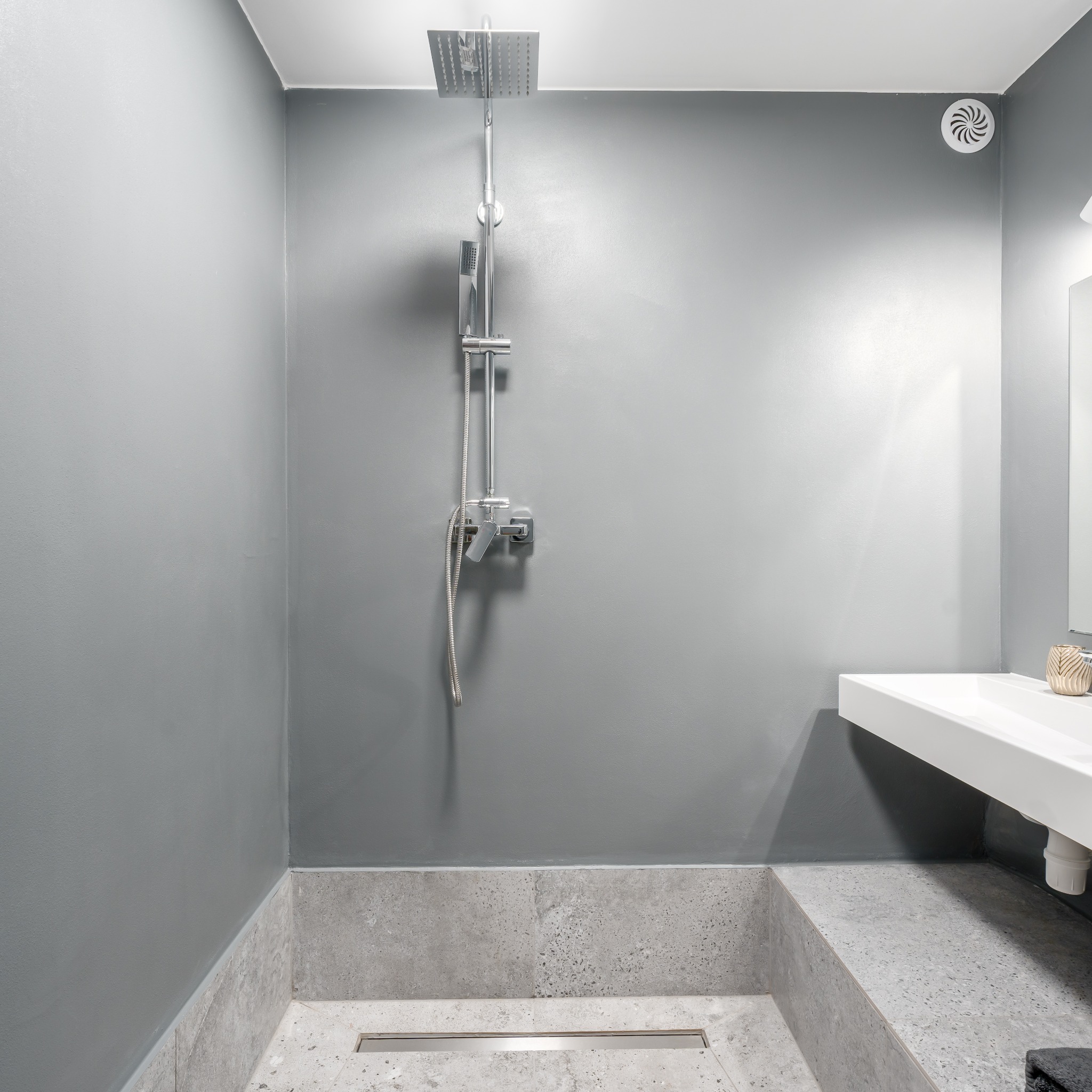 Nowoczesna łazienka w odcieniach szarości z deszczownicą, umywalką nablatową i odpływem liniowym w posadzce.