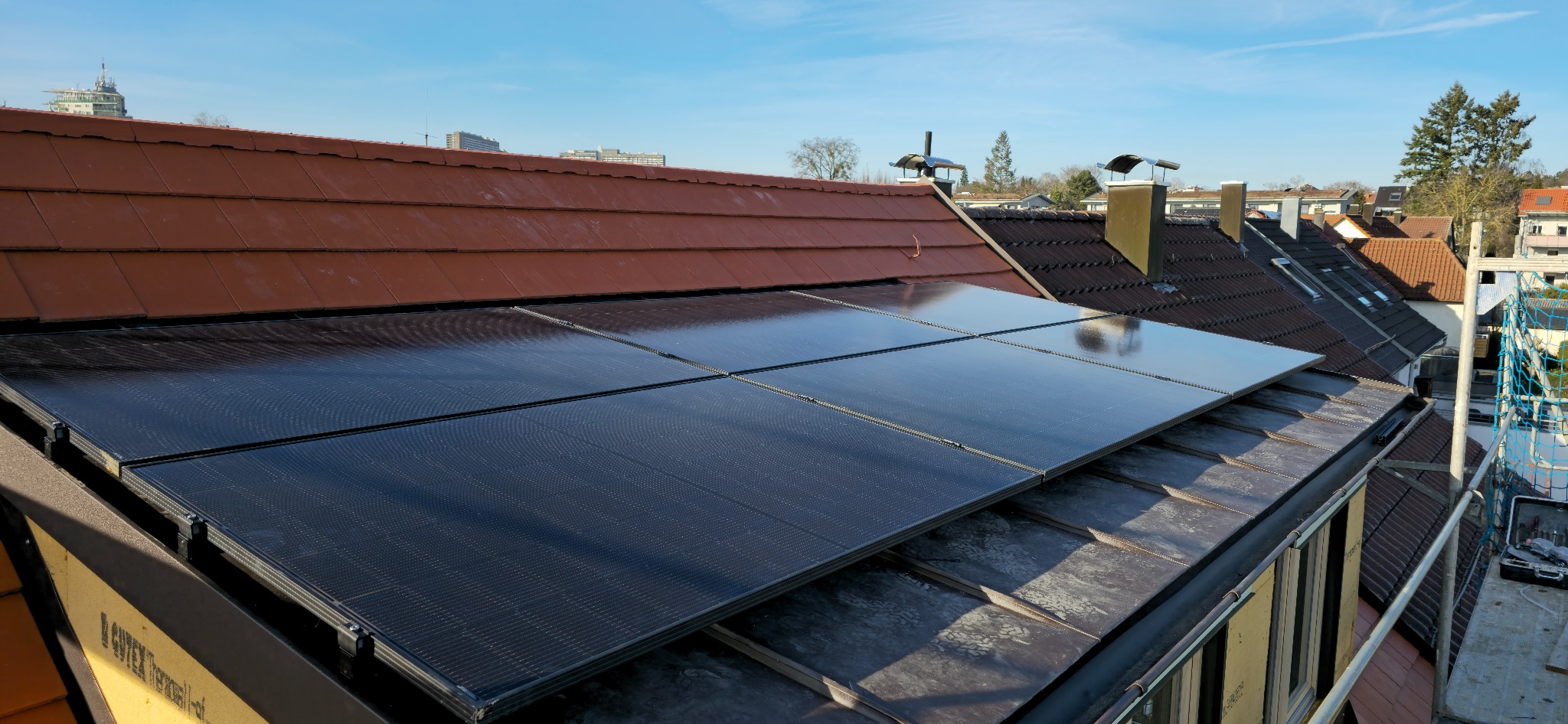 Cztery moduły fotowoltaiczne, zamontowane na dachu z czerwoną dachówką, w słoneczny dzień. Widoczne elementy montażowe i fragmenty konstrukcji dachu.