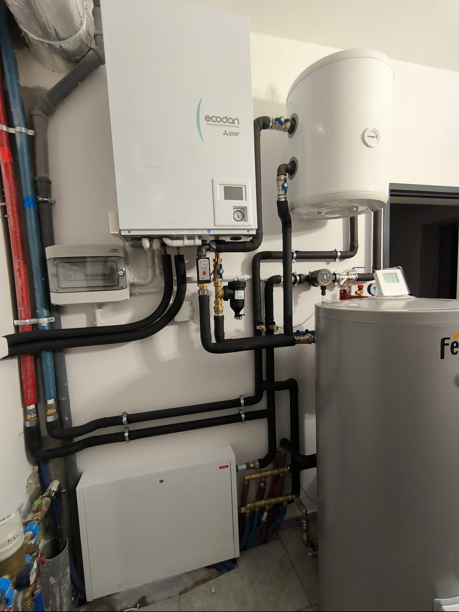 Zainstalowany, nowoczesny system grzewczy z pompą ciepła Ecodan w Białymstoku, widoczne rury w izolacji, zbiornik na wodę i rozdzielnica elektryczna.