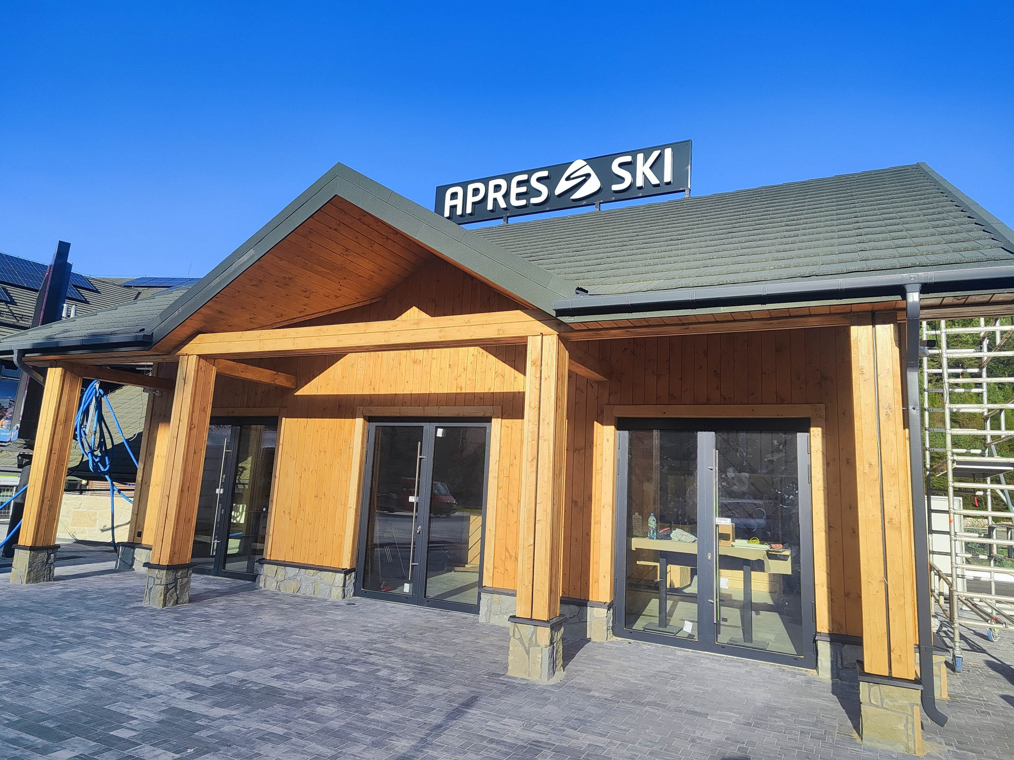 Nowo wybudowany budynek restauracji APRES SKI w Krynica-Zdrój, z drewnianą konstrukcją, kamiennymi detalami u podstawy filarów i dużym szyldem na dachu.
