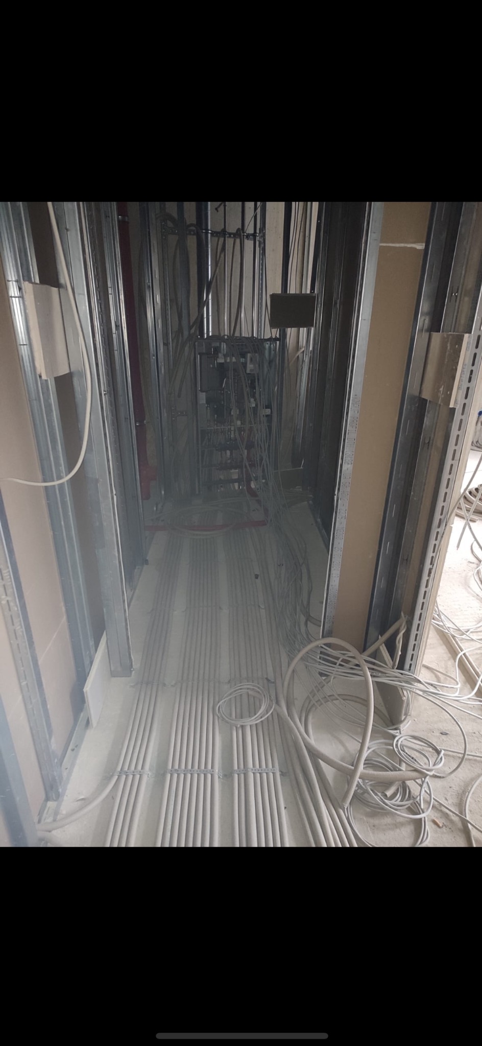 Wiązki kabli elektrycznych ułożone równolegle na podłodze w trakcie prac instalacyjnych w budynku w stanie surowym, widoczna metalowa konstrukcja ścian działowych.