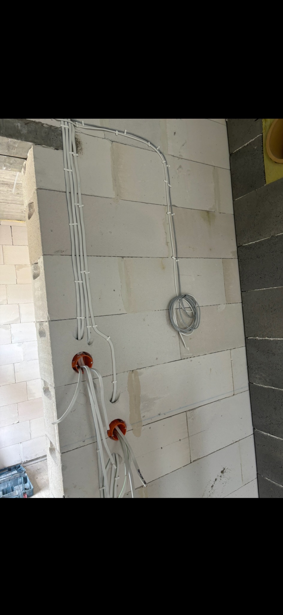 Wewnętrzne okablowanie elektryczne w surowym stanie, widoczne przewody poprowadzone po ścianie z betonu komórkowego, puszki instalacyjne w kolorze pomarańczowym, częściowo ułożone kable.
