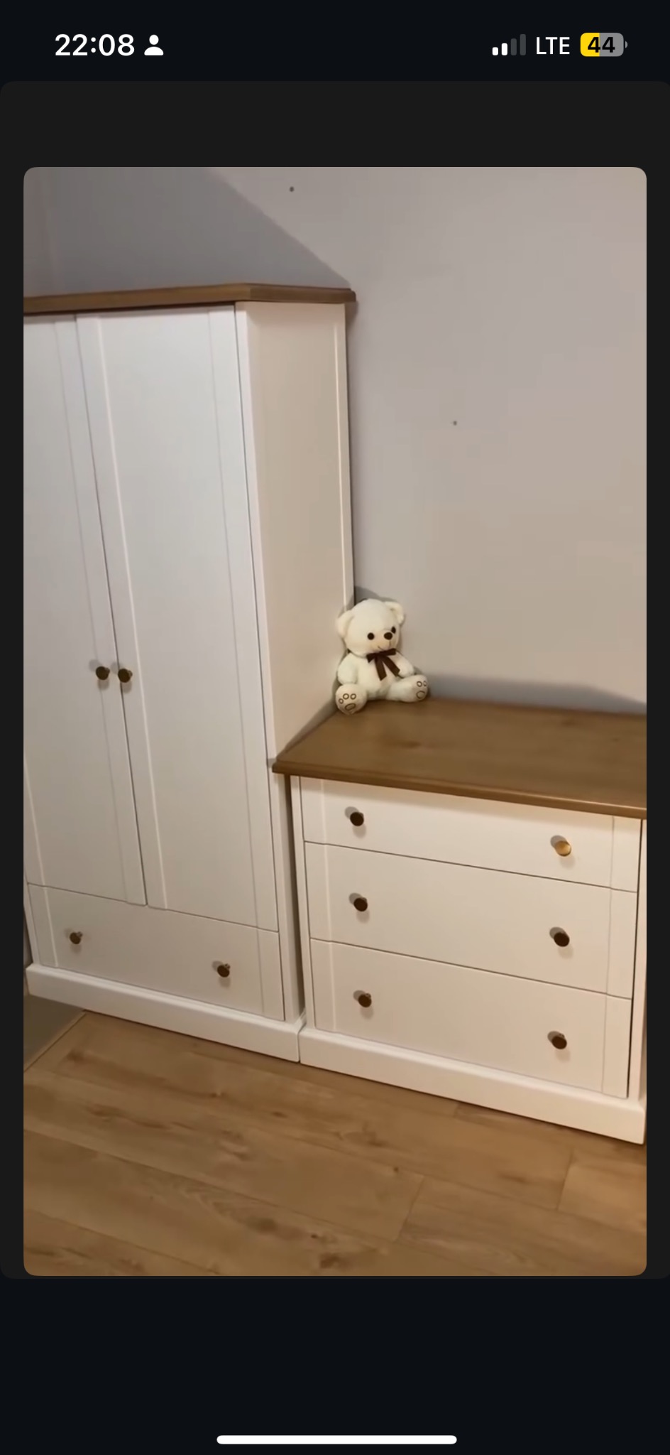 Biała szafa z drewnianym blatem i komoda z pluszowym misiem. Meble w pokoju dziecięcym, jasna podłoga. Ustawione pod ścianą.