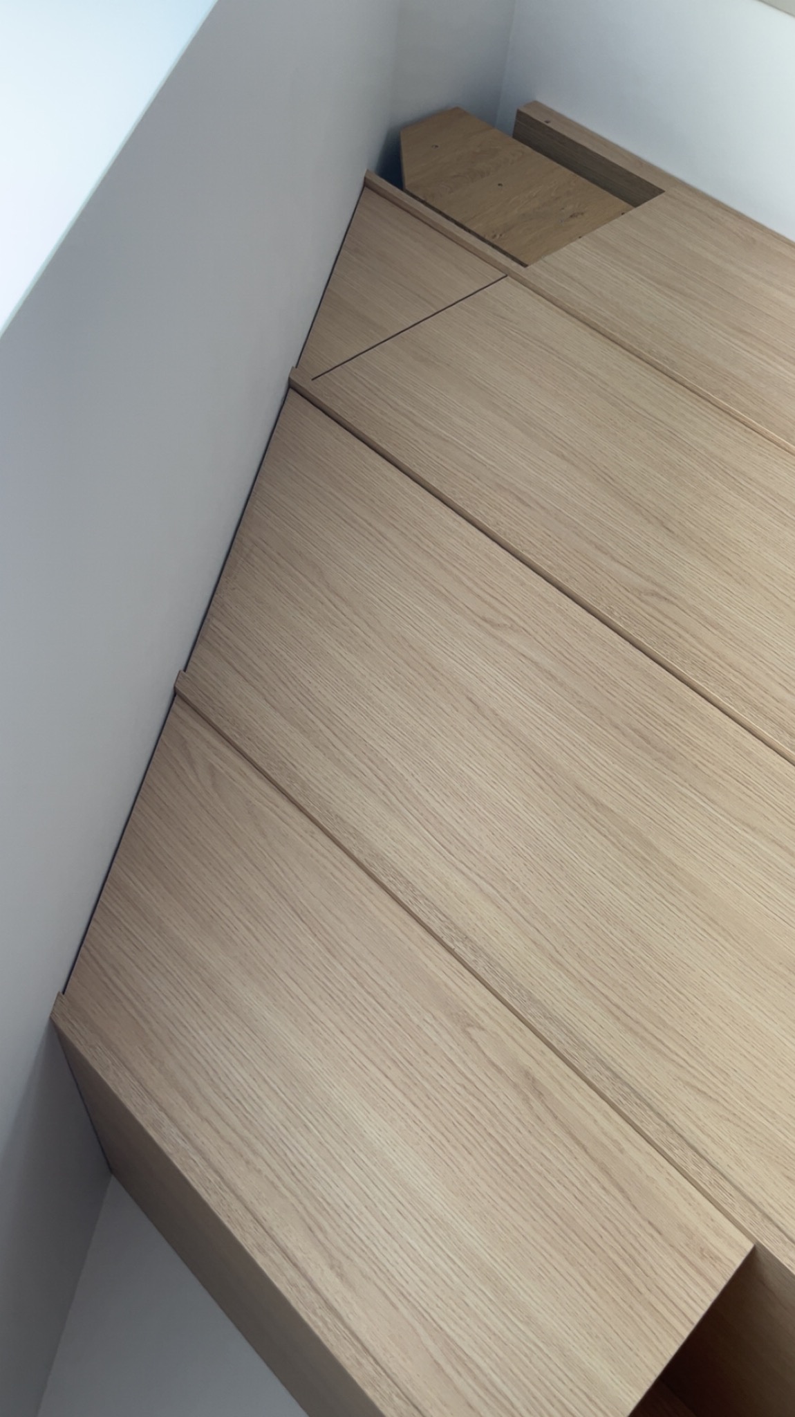 Jasne, drewniane fronty szafy wnękowej pod skosem, z widocznymi liniami podziału i fragmentem białej ściany. Minimalistyczny design, precyzyjne wykonanie.