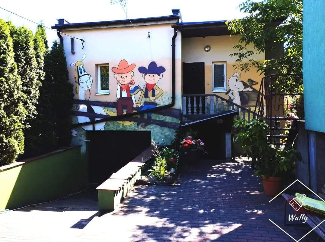 Dwupiętrowy budynek z muralami przedstawiającymi postacie z kreskówek na ścianach, w tym kowbojów i psa z ptakiem na schodach.