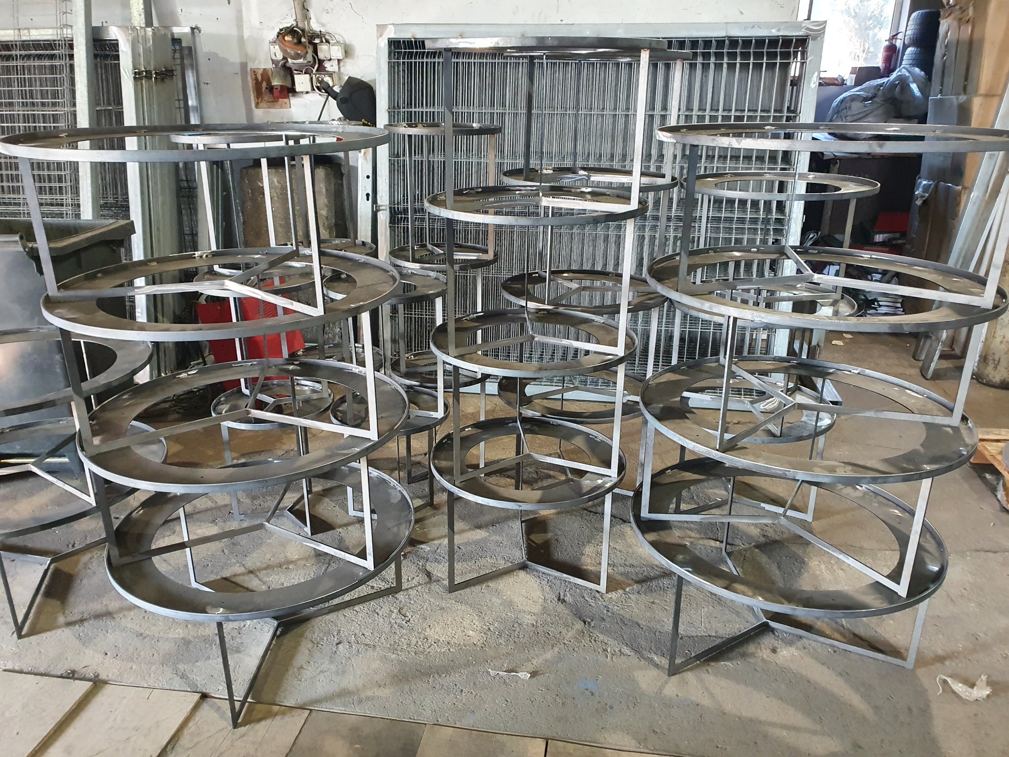 Szkielety metalowych stolików z okrągłymi blatami, wykonane przez ślusarza z Rogozina, oczekujące na dalszą obróbkę w warsztacie.
