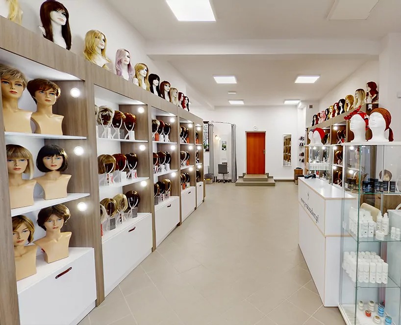 Wnętrze salonu peruk: rzędy regałów z manekinami prezentującymi różnorodne peruki, od blond po ciemne, krótkie i długie, na tle białych ścian i jasnej podłogi.