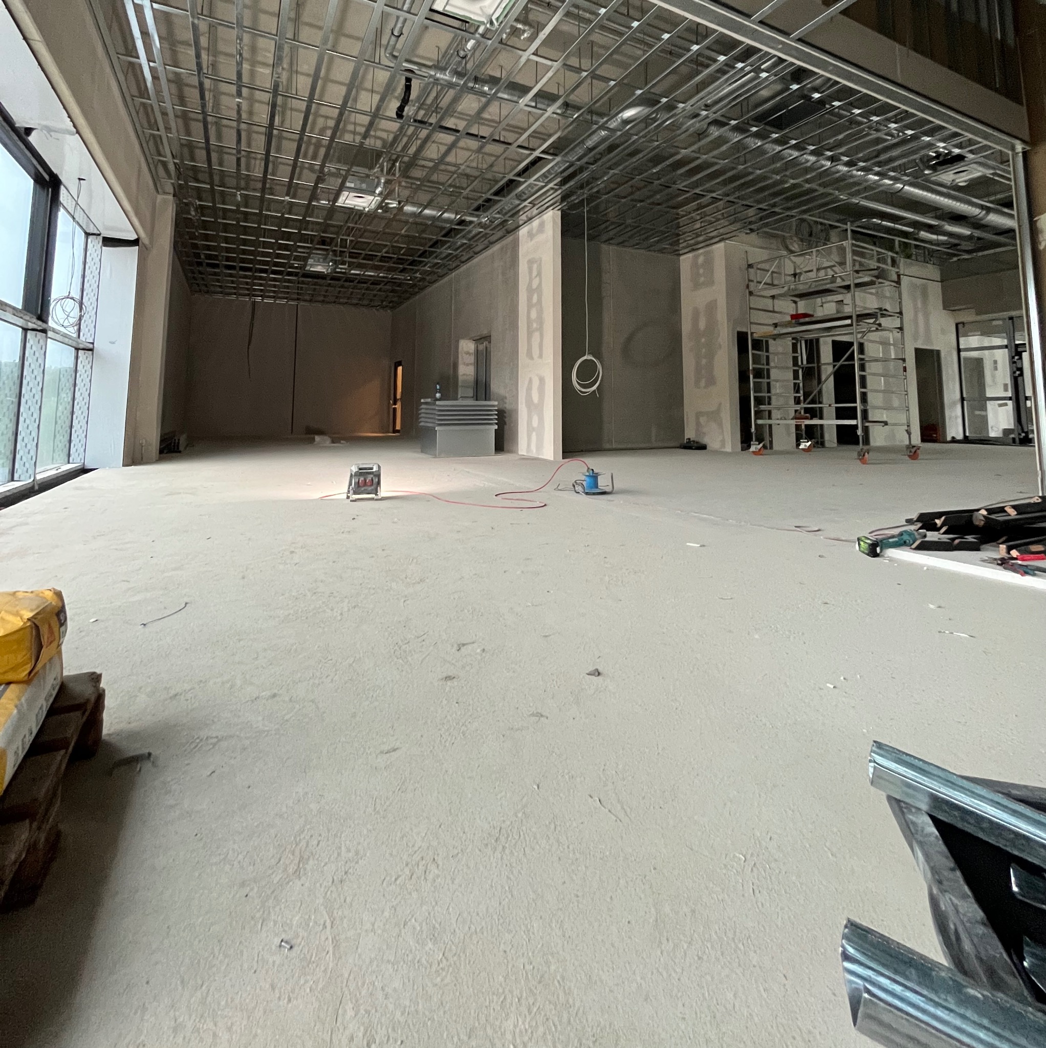Wnętrze w trakcie remontu: metalowa konstrukcja sufitu podwieszanego, ściany przygotowane pod płyty gipsowe, podłoga wylewka, rusztowanie w tle. Widok z dołu.