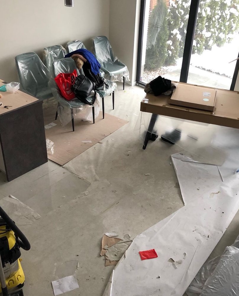 Wnętrze po remoncie: podłoga pokryta folią ochronną i resztkami gruzu, krzesła zabezpieczone folią, kartony po meblach, odkurzacz przemysłowy w rogu kadru.