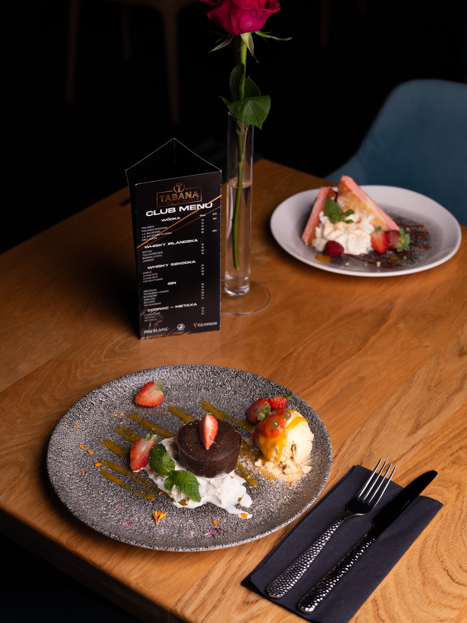 Elegancko podany deser czekoladowy z lodami i truskawkami na talerzu w restauracji w Gorzowie Wielkopolskim, obok menu i róży w wazonie.