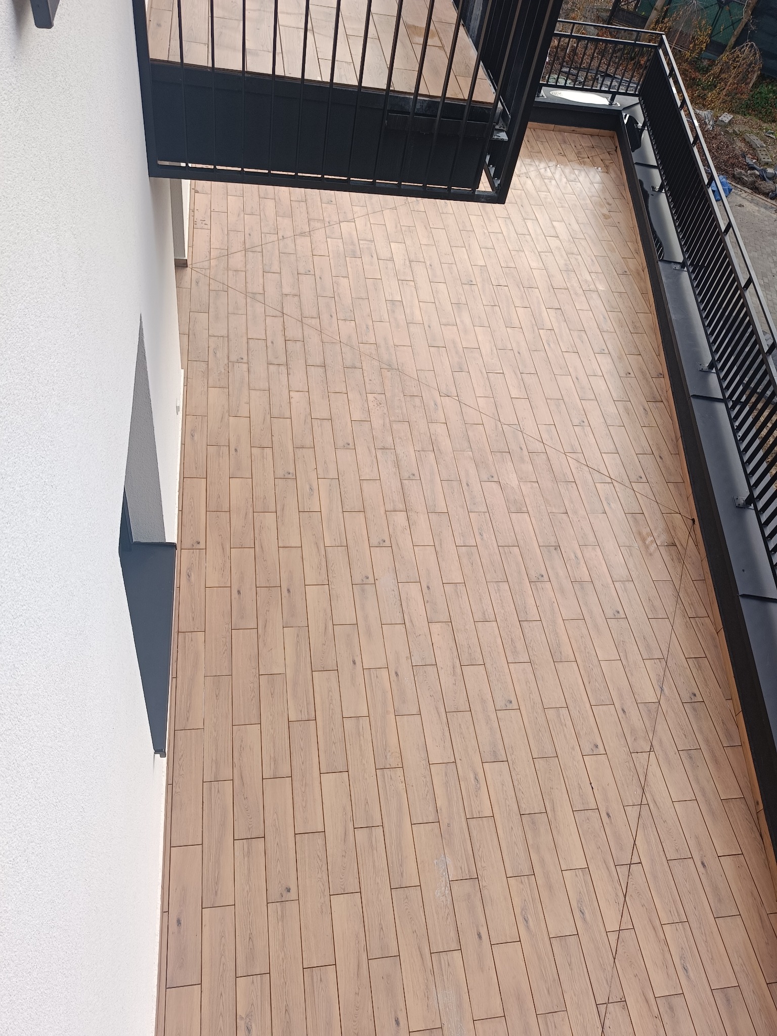 Balkon wyłożony panelami imitującymi drewno, widok z góry, czarna balustrada.