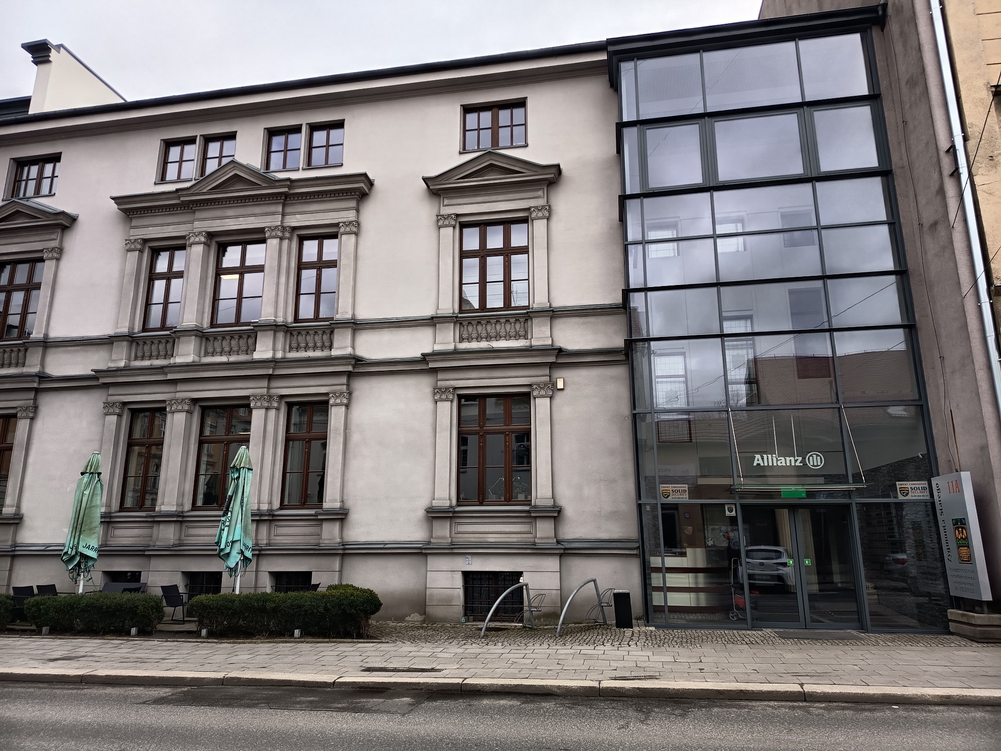 Elewacja budynku biurowego z nowoczesną szklaną fasadą i klasycznymi oknami. Widoczne logo Allianz nad wejściem.