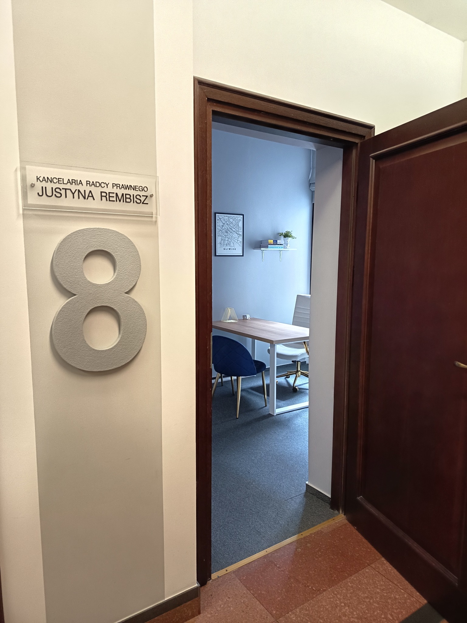 Wejście do kancelarii radcy prawnego Justyny Rembisz, numer 8, widok na wnętrze biura z biurkiem i krzesłami. Minimalistyczny wystrój, mapa Gliwic na ścianie.