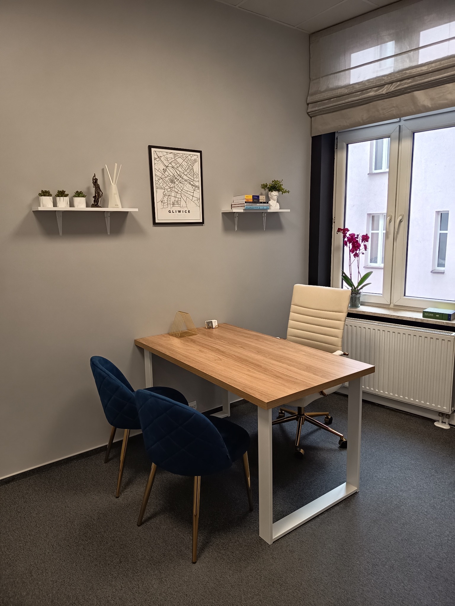 Nowoczesne biuro z drewnianym biurkiem, niebieskimi krzesłami i mapą Gliwic na ścianie. Minimalistyczny wystrój, roślina na parapecie, jasne wnętrze.
