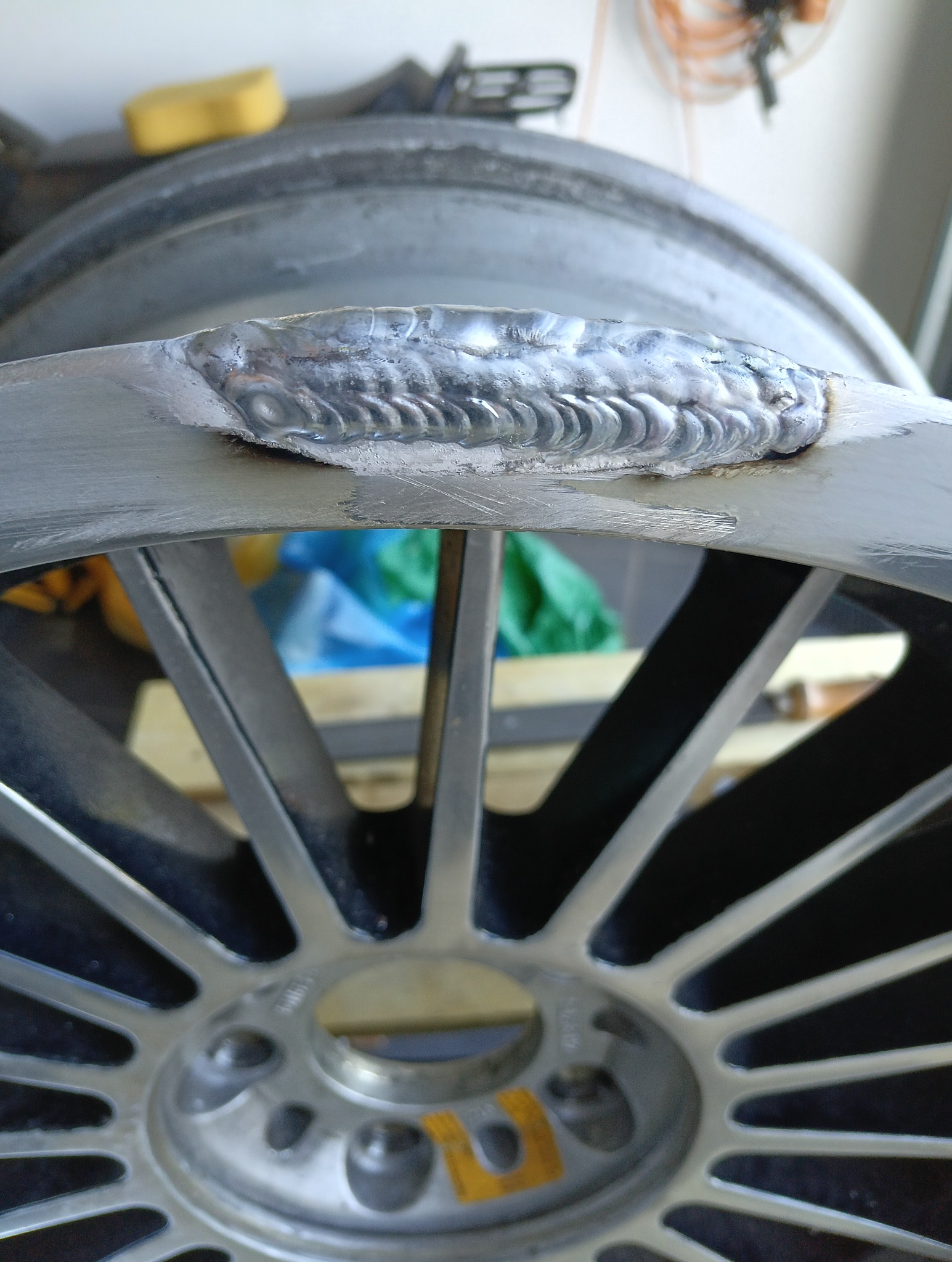 Szlif spawalniczy na obręczy aluminiowej. Widoczne ślady spawania i obróbki metalu. Obręcz z wieloma szprychami.