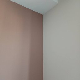 Taurus Denys Sushniak - Pomieszczenie po malowaniu: ściany w odcieniach beżu i pudrowego różu, widoczne łączenie ścian i sufitu. Minimalizm, gładkie powierzchnie, brak dekoracji.