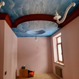 Taurus Denys Sushniak - Pokój po malowaniu ścian na różowo i artystycznym malowaniu sufitu w błękitne chmury. Widoczne dekoracyjne elementy oświetleniowe i wykończeniowe.
