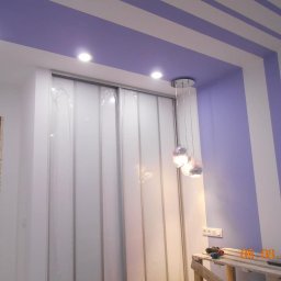 Taurus Denys Sushniak - Pomalowany sufit z pasami i ścianą w odcieniach fioletu, białe drzwi przesuwne z folią ochronną, lampa wisząca i fragment rusztowania ze śladami pracy.