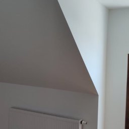 Taurus Denys Sushniak - Białe wnętrze poddasza po remoncie: skośny sufit, ściany pomalowane na biało, grzejnik i panele podłogowe w odcieniach brązu. Minimalistyczny design.