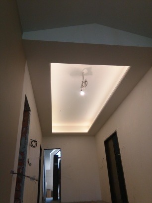 Korytarz po remoncie z podwieszanym sufitem z oświetleniem LED. Widoczne przygotowane otwory drzwiowe i świeżo pomalowane ściany w neutralnym odcieniu.