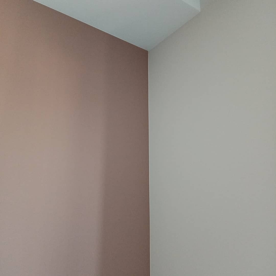 Pomieszczenie po malowaniu: ściany w odcieniach beżu i pudrowego różu, widoczne łączenie ścian i sufitu. Minimalizm, gładkie powierzchnie, brak dekoracji.
