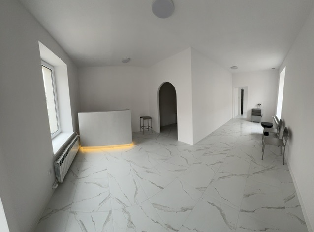 Białe, minimalistyczne wnętrze po remoncie z marmurową podłogą, podświetlaną recepcją i metalowymi krzesłami.