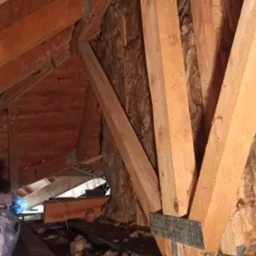 Drewniana konstrukcja dachu z izolacją z wełny mineralnej, widoczna z perspektywy poddasza w Chobieni. Elementy wzmocnione metalowymi łącznikami.