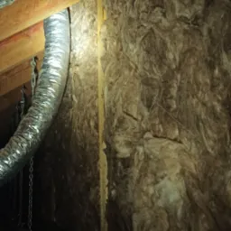 Izolacja poddasza wełną mineralną, widoczne przewody wentylacyjne aluminiowe i drewniana konstrukcja dachu.