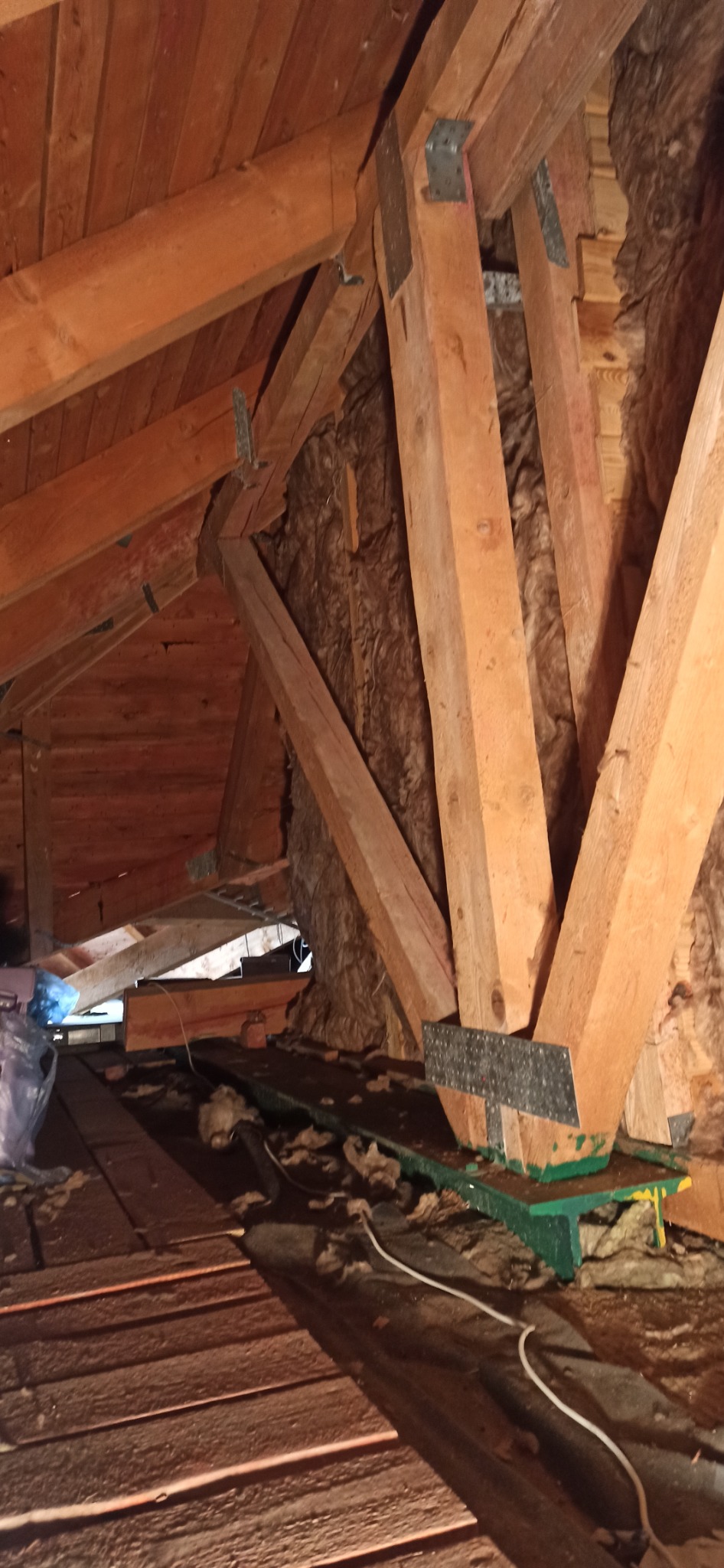 Drewniana konstrukcja dachu z izolacją z wełny mineralnej, widoczna z perspektywy poddasza w Chobieni. Elementy wzmocnione metalowymi łącznikami.