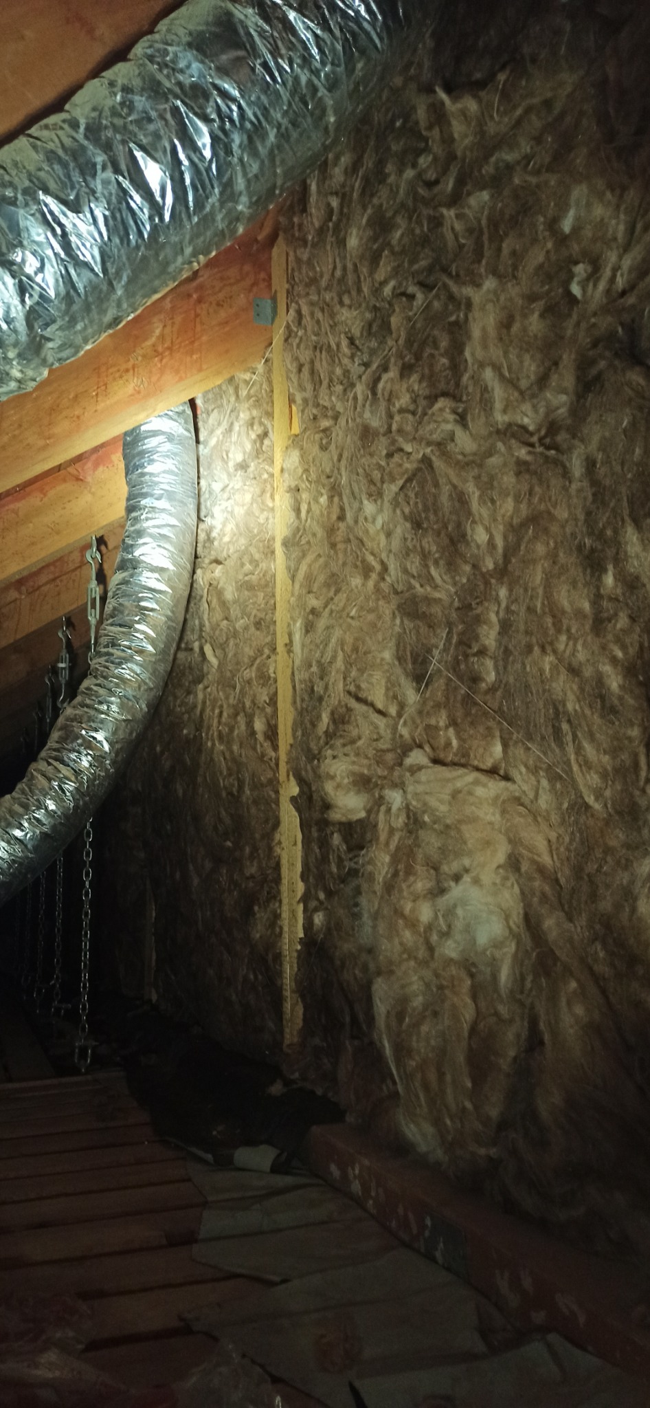 Izolacja poddasza wełną mineralną, widoczne przewody wentylacyjne aluminiowe i drewniana konstrukcja dachu.