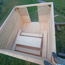 OLEKSANDR SMERECHUK PraceBud - Wysoka perspektywa na drewnianą altanę z kratownicą, częściowo zmontowaną, z widocznymi deskami podłogowymi i elementami konstrukcyjnymi. Podłoże trawiaste.