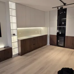 Nowoczesna kuchnia z białymi górnymi szafkami i drewnianymi dolnymi, zintegrowany piekarnik i chłodziarka do wina, oświetlenie LED podszafkowe, minimalistyczny zlew i bateria, oraz dekoracyjny klon...