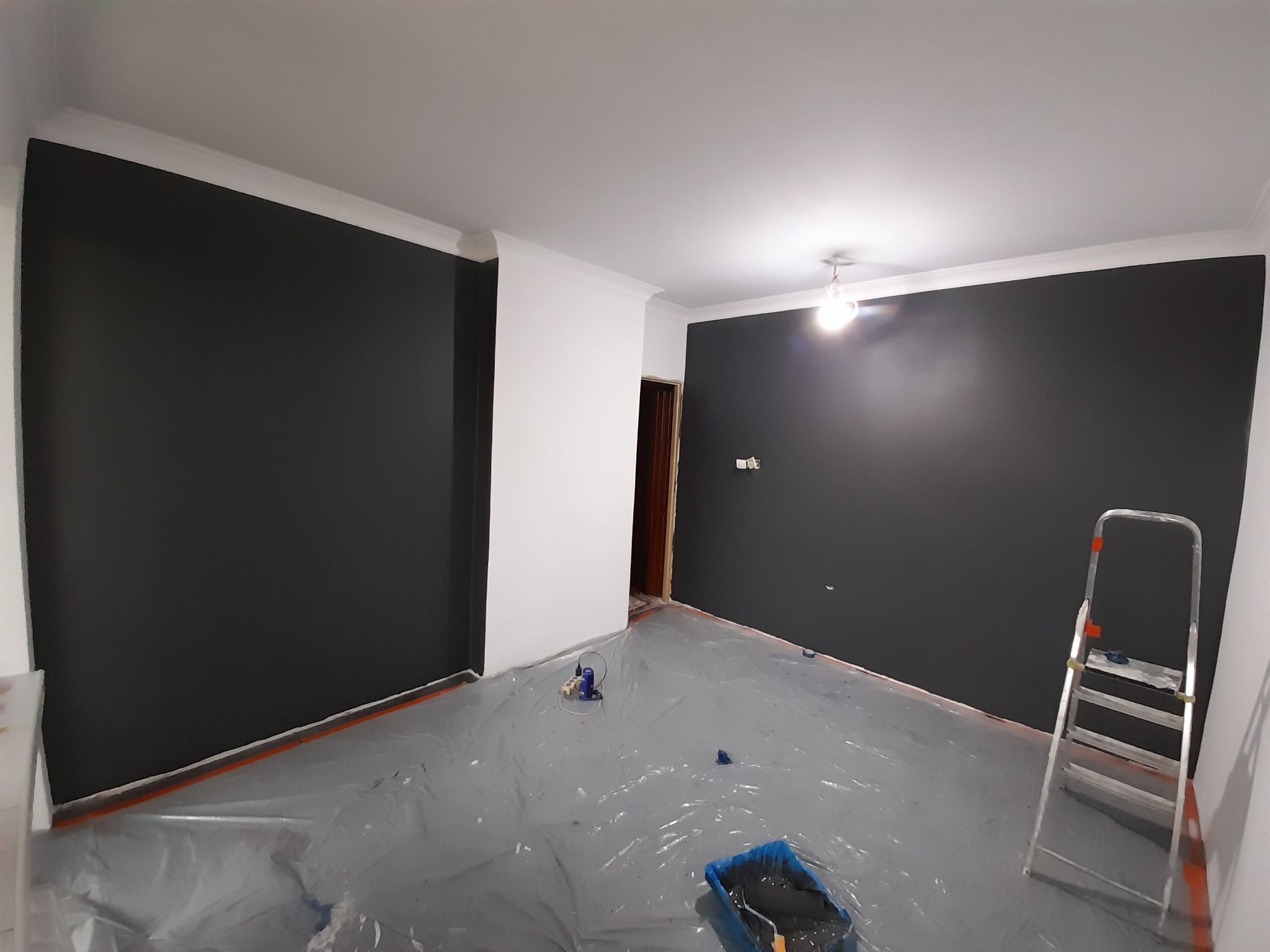 Pokój w trakcie malowania na ciemny grafit, zabezpieczona folią podłoga, widoczna drabina malarska i kuweta z farbą.