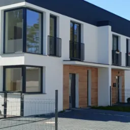 Nowoczesny segment bliźniaka z dużymi oknami z czarnymi ramami, balkonami z czarnymi balustradami i elewacją z elementami drewnopodobnymi.