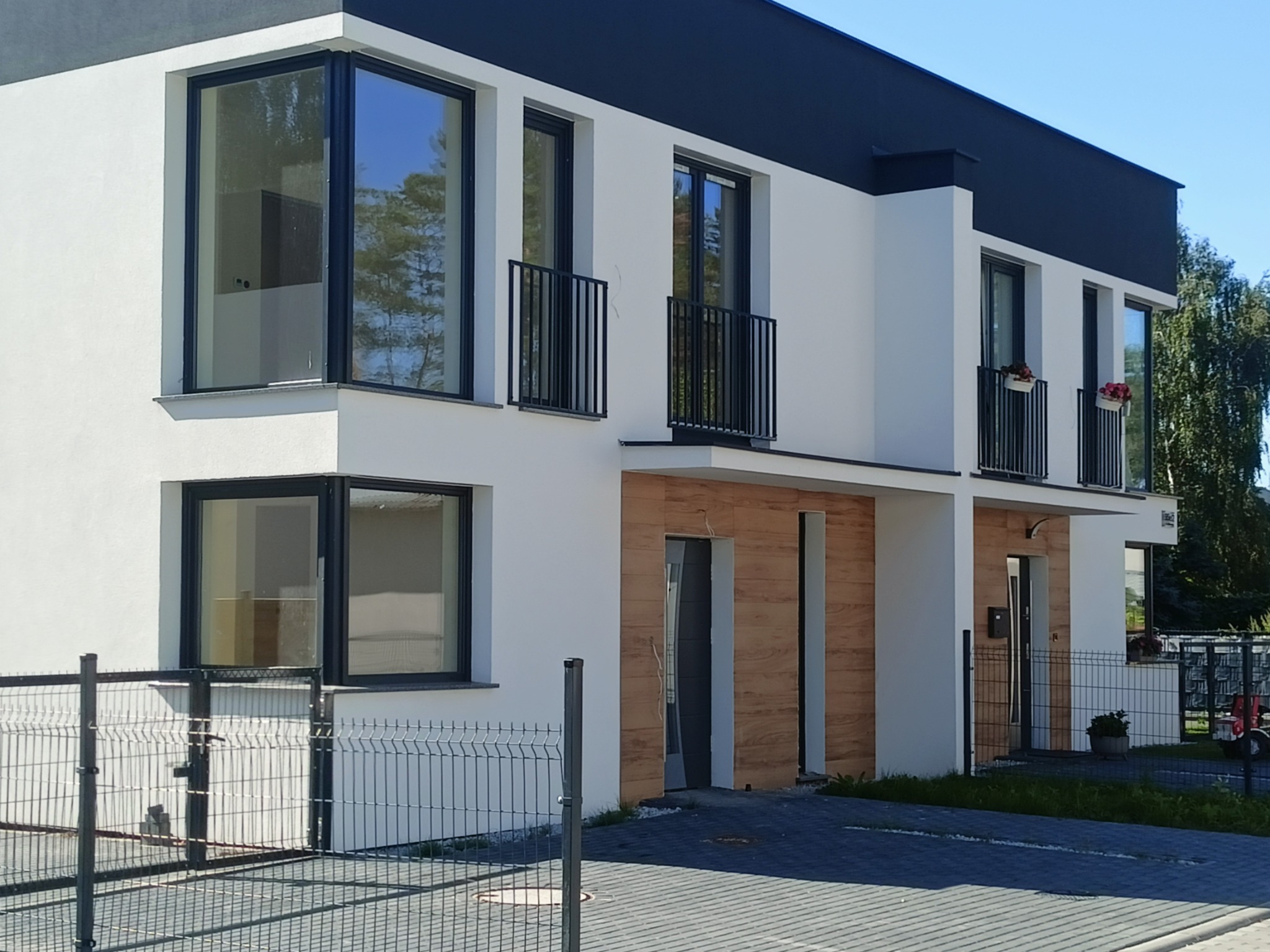 Nowoczesny segment bliźniaka z dużymi oknami z czarnymi ramami, balkonami z czarnymi balustradami i elewacją z elementami drewnopodobnymi.