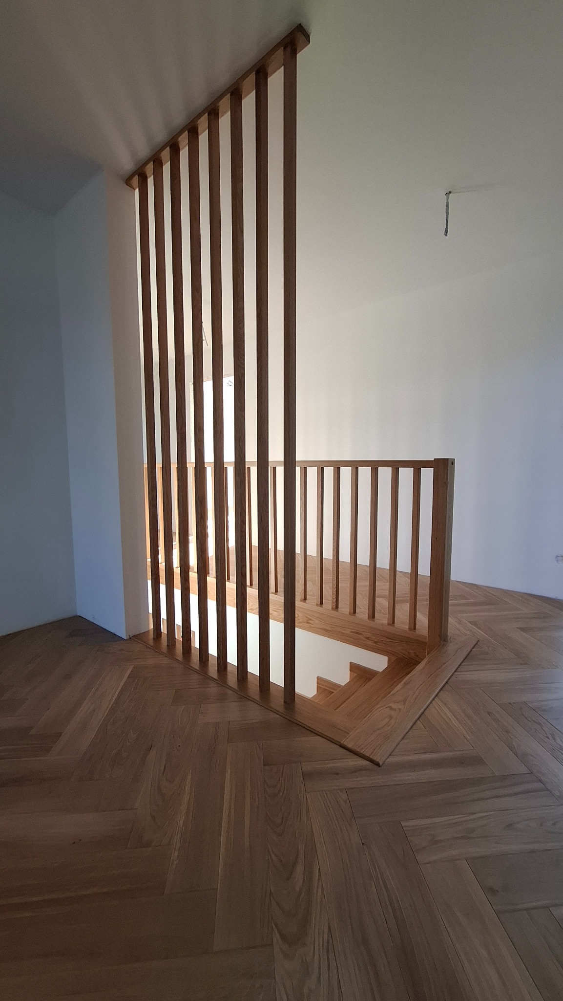 Nowoczesna drewniana balustrada schodowa z pionowymi szczeblami i podłogą w jodełkę, widok z góry.