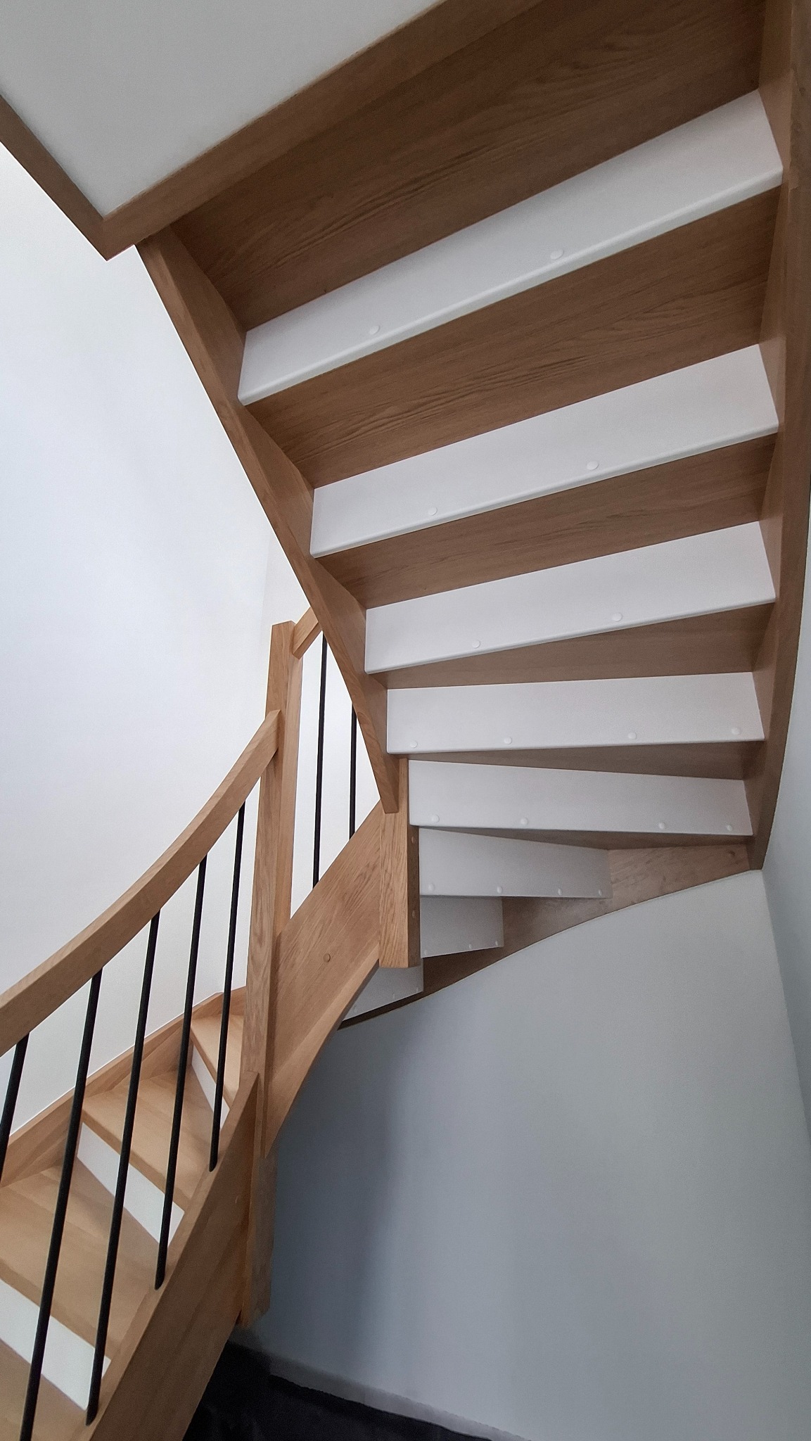 Drewniane schody z czarnymi poręczami, widok od dołu, stopnie wykończone białymi podstopnicami.