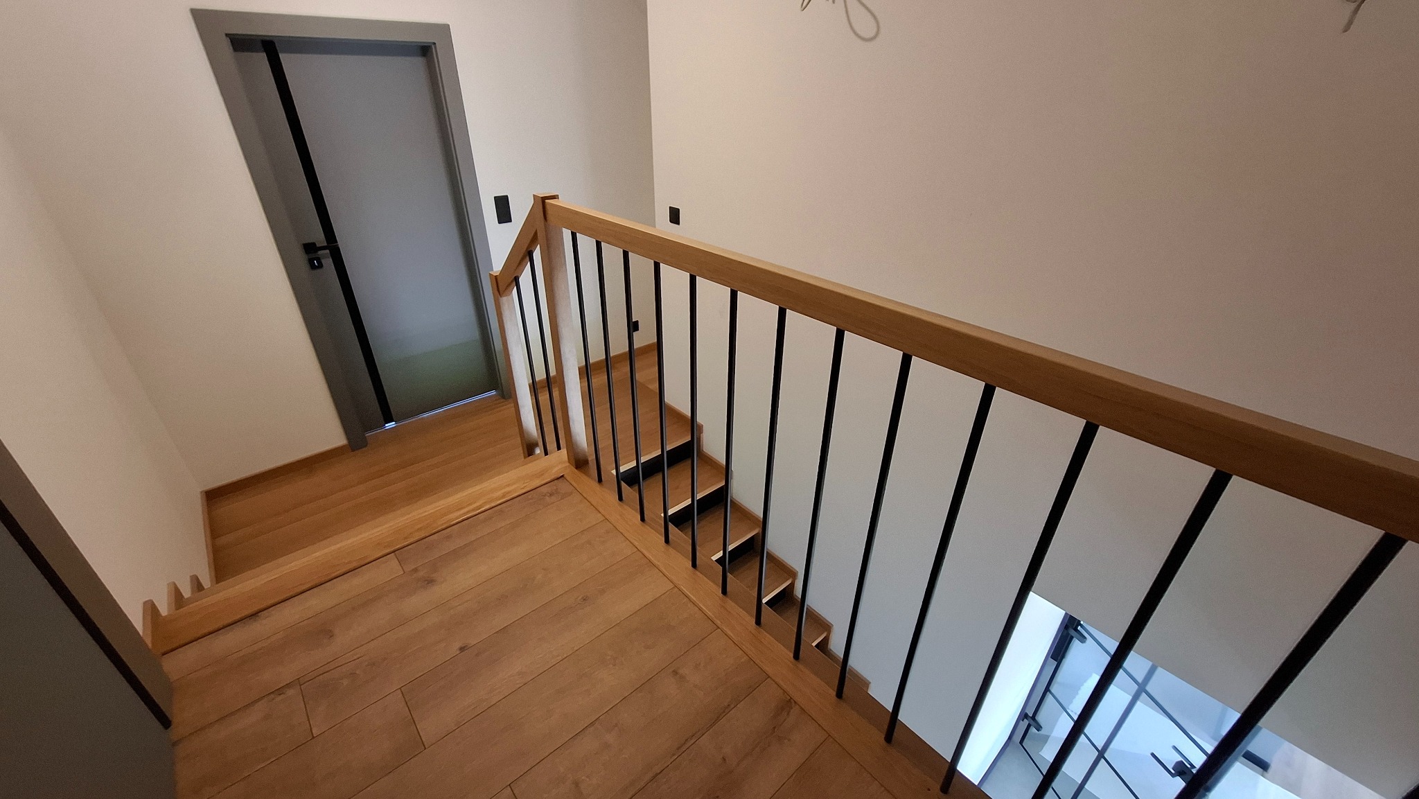 Klatka schodowa z drewnianymi stopniami i poręczą z czarnymi, metalowymi prętami w nowoczesnym domu.