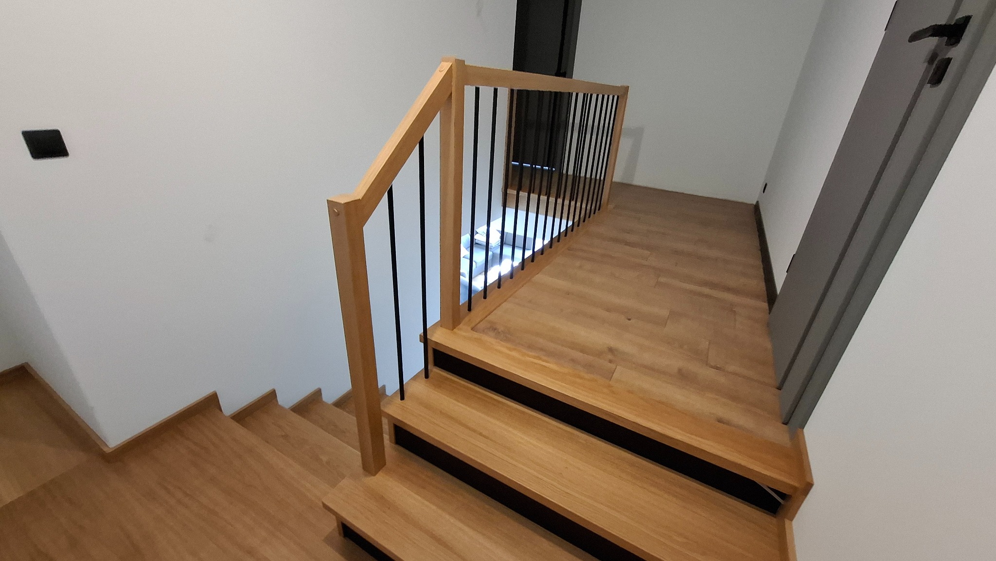 Jasne drewniane schody z czarnymi metalowymi balustradami, widok z góry, minimalistyczny design.