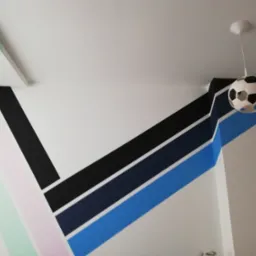 Pokój dziecięcy z geometrycznym malowaniem ścian w odcieniach pastelowych i niebieskich, uzupełniony lampą sufitową w kształcie piłki nożnej.