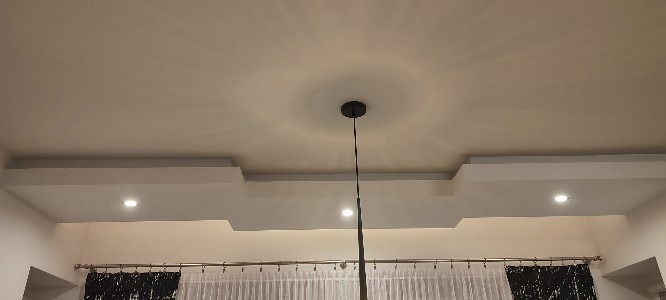 Nowoczesny sufit podwieszany z oświetleniem punktowym i centralną lampą wiszącą z czarnym kablem, widok od dołu.