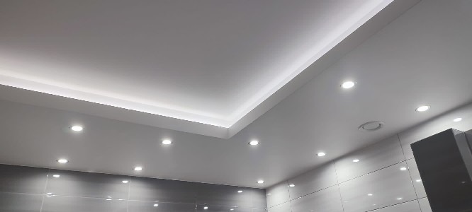 Nowoczesna łazienka z podwieszanym sufitem z oświetleniem LED i punktowymi lampami, szare płytki na ścianach.